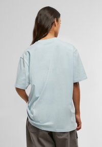 Gaiši zils kokvilnas T-krekls ar brīvu piegriezumu, īsām piedurknēm un apaļu kakla izgriezumu, kas izceļas ar gludu tekstūru un minimālu dizainu.