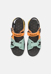 Timberland sandaalit, joissa on mintunvihreä päällinen, oransseja ja mustia yksityiskohtia, säädettävät hihnat ja kuusikulmainen musta pohja.
