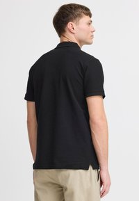 Sort polo-shirt med korte ærmer, lavet af glat stof, med en delt kant og tekstureret krave. Standard pasform, minimal design.