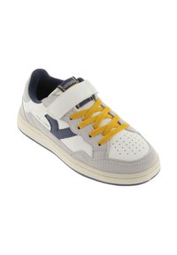 Zapatilla blanca y gris con cordones amarillos, materiales de ante y cuero, tiras de velcro, puntera perforada y acentos azul marino en los laterales.