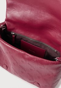 Burgunderfarvet læderhåndtaske med præget geometrisk mønster, magnetisk lukning og indvendig lynlås-lomme. Glat overflade og detaljer i sølvhardware.