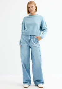 Suéter de punto azul claro con dobladillo acanalado, combinado con pantalones cargo de denim azul claro de corte holgado que cuentan con bolsillos laterales y una silueta relajada.
