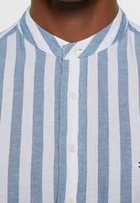 Camicia a righe blu chiaro e bianca con colletto alla coreana, dotata di chiusura con bottoni e tessuto grattato.