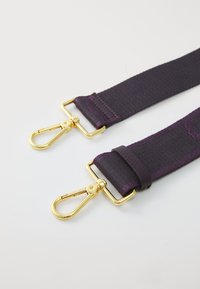 Bande en tissu violet avec une finition texturée, dotée de clips en métal doré aux deux extrémités pour l'attachement. Design durable et réglable.