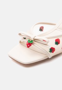 Sandale crème à bout carré, broderie de fraise, et un nœud orné d'un charm de fraise perlé sur le dessus.