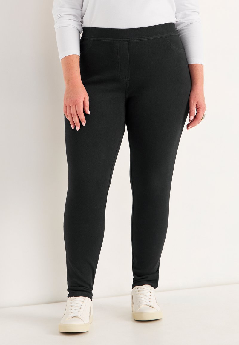 Zwarte leggings met een gladde textuur en een aansluitend ontwerp. Heeft een elastische tailleband en minimale stikseldetails. Draagt met witte sneakers.