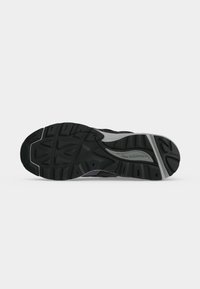 Σόλα από μαύρο και γκρι αθλητικό παπούτσι New Balance με υφή πέλματος και εμφανές όνομα της μάρκας στη μέση.