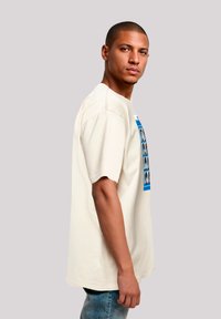 Cream short-sleeve t-shirt featuring a graphic print of various faces in blue frames. Made from soft fabric, relaxed fit, with a round neckline.