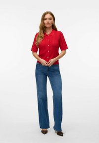 Röd kortärmad skjorta med krage och ribbad struktur, i kombination med högmidjade blå vida jeans och bruna skor.