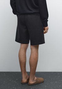Zwarte katoenen shorts met een rechte snit, voorzien van een eenvoudige tailleband en zijzakken, gedragen met bruine suède instapschoenen.