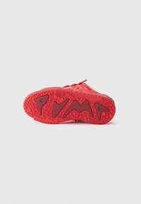 Sneaker rosso brillante visto dalla suola, con grip testurizzato e motivi di battistrada geometrici astratti su uno sfondo bianco.