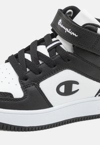 Baskets montantes noir et blanc avec de gros lacets noirs, bride de marque Champion et logo Champion sur le panneau latéral.