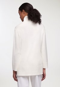 Maglione bianco con colletto alto, maniche lunghe e polsini a coste. Texture morbida, vestibilità rilassata e orlo posteriore più lungo. Finitura liscia.