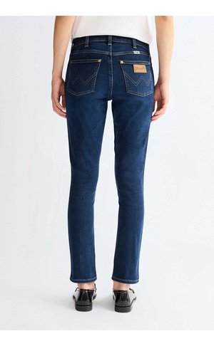 Osoba nosząca ciemnoniebieskie jeansy typu slim-fit z tylnymi kieszeniami i czarne buty, stojąca na jednolitym jasnym tle.