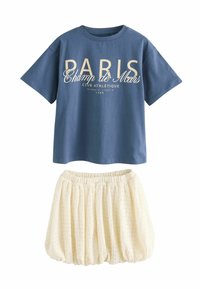 T-shirt en coton bleu avec l'inscription "PARIS" et "Champ de Mars", associé à une jupe texturée crème avec une taille élastique.