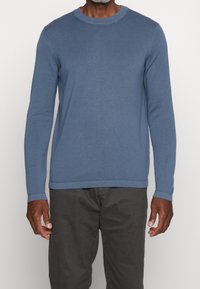 Maglione blu a maniche lunghe realizzato in un tessuto morbido, caratterizzato da un colletto rotondo, una texture a costine e un logo ricamato discreto sul petto.
