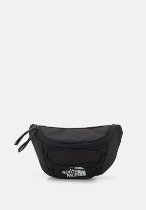 Sort North Face talletaske med lynlås-lukninger, elastisk frontdetalje og logo printet på frontlommen mod en ensfarvet lys baggrund.