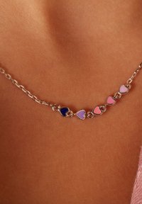 Zilveren ketting met afwisselend harten in paarse en roze tinten, tegen een gladde huidskleurige achtergrond.