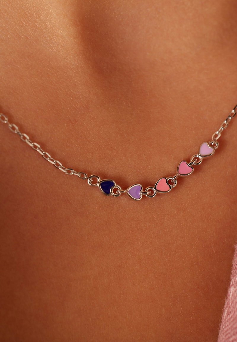 Zilveren ketting met afwisselend harten in paarse en roze tinten, tegen een gladde huidskleurige achtergrond.