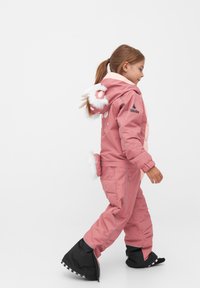 Roze kindersneeuwpak met witte nepbontaccenten op de capuchon, konijnenoren en een staart, waterdicht materiaal en zwarte laarzen met witte rand.