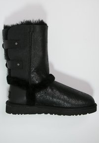 Botte noire montant jusqu'au genou en cuir texturé avec bordure en fausse fourrure. Dispose de deux sangles ajustables avec des finitions métalliques. Semelle en caoutchouc pour une meilleure adhérence.