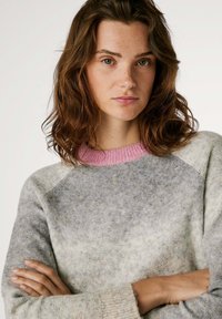 Suéter de punto con un diseño en degradado en gris y un escote acanalado rosa. La textura parece suave con un corte holgado y mangas raglán.