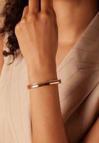 Roze gouden armband met een gladde, gepolijste afwerking en een kanaal van ingebedde heldere stenen. Verstelbare pasvorm, slank ontwerp.