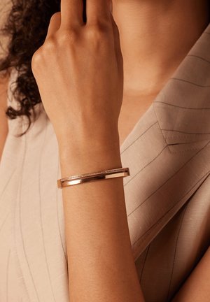 Roze gouden armband met een gladde, gepolijste afwerking en een kanaal van ingebedde heldere stenen. Verstelbare pasvorm, slank ontwerp.