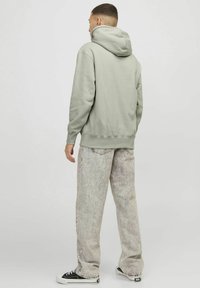 Sudadera verde claro con un bolsillo tipo canguro, puños elásticos y dobladillo; combinada con unos jeans claros y texturizados y zapatillas negras.