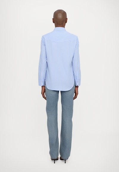 Blau-weiß gestreiftes Hemd mit Button-Down-Kragen, langen Ärmeln und leicht abgerundetem Saum, kombiniert mit Schlagjeans.