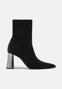 Črne tkaninske gležnjarje s koničastim nosom in kovinskim blokom peto. Brezhibna tekstura in brezšiven dizajn z vidnimi šivi.