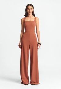 Rostfärgad jumpsuit med fyrkantig halsringning, vida ben och tjocka axelremmar. Slät tygkvalitet, med framfickor och skräddarsydd passform.