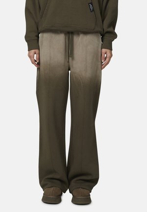 Pantaloni jogging verde oliva con un design sbiadito, vita regolabile con cordino, gambe larghe e cuciture in evidenza, abbinati a calzature marroni.
