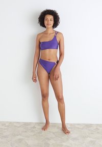 Purple bikini set featuring a one-shoulder top and high-waisted bottom with a ring accent. Smooth texture and fitted design.