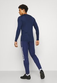 Marineblauw sportief longsleeve shirt met een slim fit ontwerp, gecombineerd met bijpassende marineblauwe joggers met witte zijstrepen en zwarte sportschoenen.