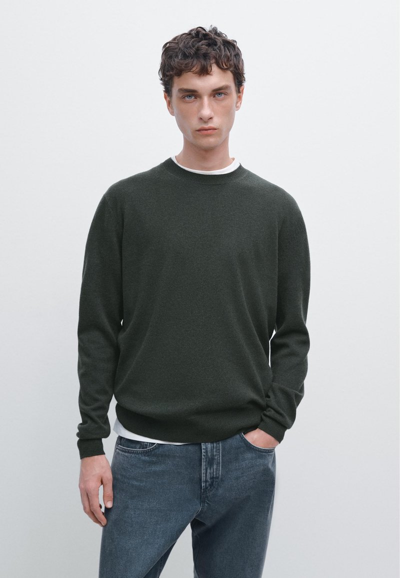 Donkergroene gebreide trui met een ronde hals, lange mouwen en een losse pasvorm, gecombineerd met blauwe denim jeans.