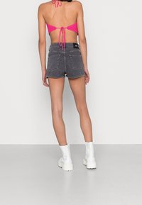 Shorts de mezclilla negros de talle alto, con puños deshilachados y bolsillos traseros. Combinados con una blusa rosa brillante con lazo en la espalda y elegantes botas blancas hasta el tobillo.