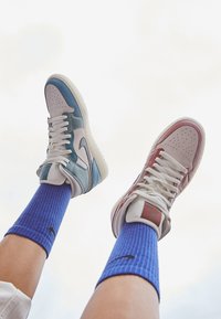 High-top sneakers met gemengde materialen in teal, roze en crème. Witte zolen en grijze veters. Blauwe geribbelde sokken met zwart logo.