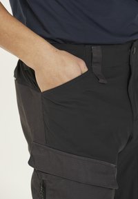 Svarta cargobyxor med en sidoficka och en slät textur. Har en sydd midja och en hand i fickan.