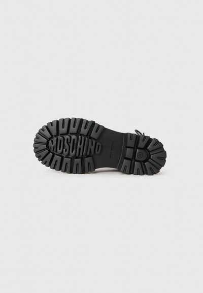Mustmustest musta jalatsite alla äärmiselt tekstuuriga pind, sügavate soontega ja "MOSCHINO" brändimisega. Tugev ja vastupidav disain.