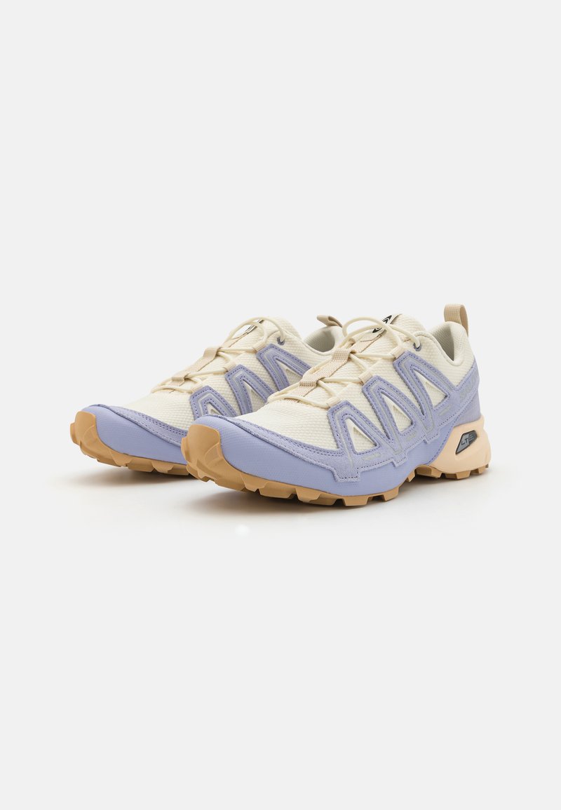 Sportschuhe mit einer Farbkombination aus Creme und Lavendel, ausgestattet mit einer strukturierten Oberseite, Netzpaneelen, ausgeprägten Details und einer Gummisohle.