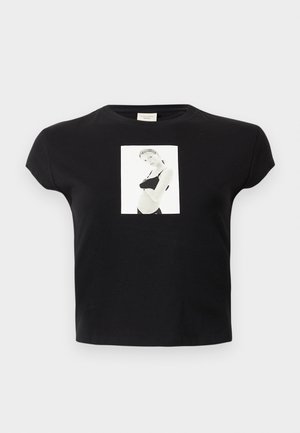 Zwart cropped t-shirt met korte mouwen, met een centrale witte grafiek waarop een zwart-wit foto van een vrouw in een beha en broek die zijwaarts poseert staat.