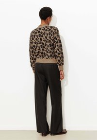 Pull beige avec imprimé léopard noir, poignets et ourlet côtelés ; assorti à un pantalon large noir taille haute, en tissu texturé.