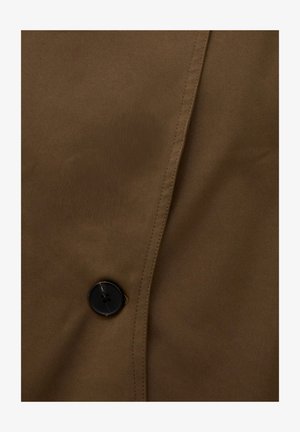 Close-up of a brown fabric with a black four-hole button sewn near the center and visible stitching along the edge.