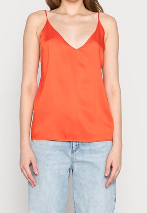 Czerwony satynowy top na cienkich ramiączkach z dekoltem w kształcie litery V, o gładkiej fakturze i luźnym kroju, zestawiony z jasnoniebieskimi jeansami.
