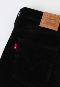 Μαύρο παντελόνι Levi's από κοτλέ υλικό που δείχνει την πίσω τσέπη, κόκκινη ετικέτα Levi's και καφέ δερμάτινο λογότυπο με κείμενο.