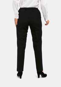 Zwarte, op maat gemaakte broek met rechte pijpen, elastische tailleband en zijzakken. Draagt een wit hemd met lange mouwen en zwarte hakken.