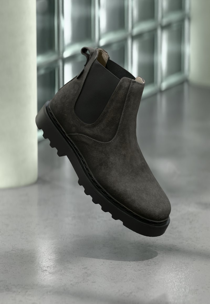 Stivaletto Chelsea in camoscio grigio scuro con pannelli laterali elastici neri e suola spessa nera con carrarmato su pavimento riflettente in cemento.