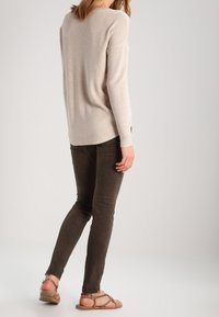 Light beige knit sweater with long sleeves, paired with dark brown fitted jeans. The outfit includes tan flat sandals.