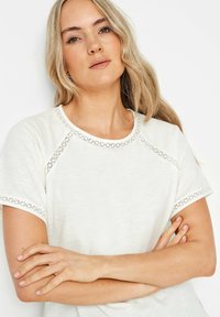 T-shirt bianco in cotone con maniche corte, presenta un bordo decorativo in pizzo grigio sul collo e sui orli delle maniche, vestibilità rilassata.